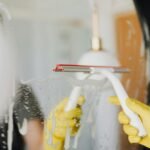 Person using a squeegee to clean a foamy bathroom mirror indoors.